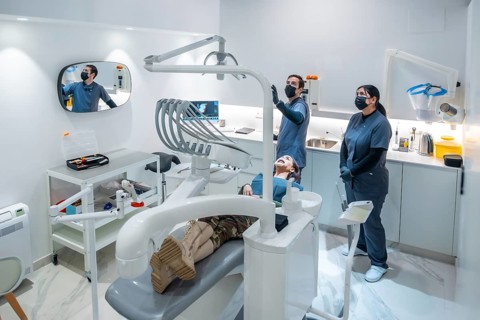 Two dentists wearing face masks showing a patient the results of a teeth whitening treatment on a