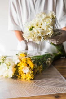 Woman florist wearing gloves carefully wraps an arrangement of white and yellow flowers at a floral