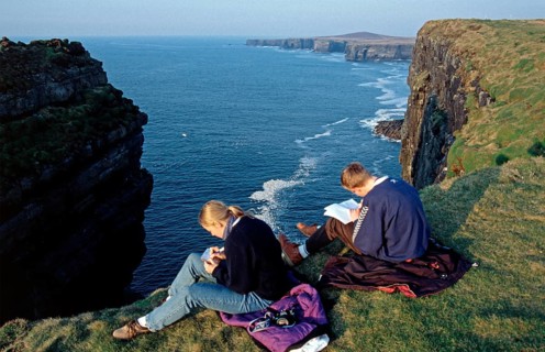 Woman and teenager writing postcard and diary, cliffs near Kilkee, County Clare, Republic of