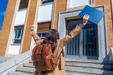 Student with backpack and folder raising arms in triumph, celebrating achievement and education