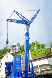A large blue construction crane in front of a modern building under a cloudy sky, Hermann Hesse