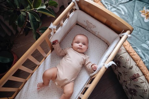 Adorable baby boy lying in a crib with soft bedding. The cozy setting features a wooden crib and a
