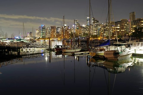 Boat and skyscrapers reflected in the calm harbour water, night shot, Stanley Park, Vancouver,