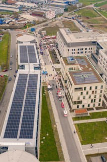 Crowd gathers between modern buildings with solar panels, opening hospital, Calw, Germany