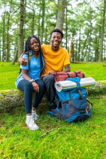 Vertical portrait of young african friends embracing sitting on a log together in a green forest in