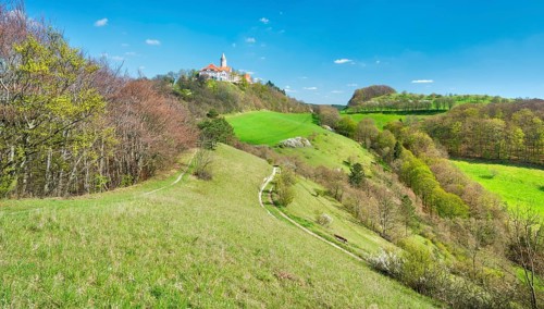 View of hilly landscape with green meadows and forests in spring, hiking trails lead to