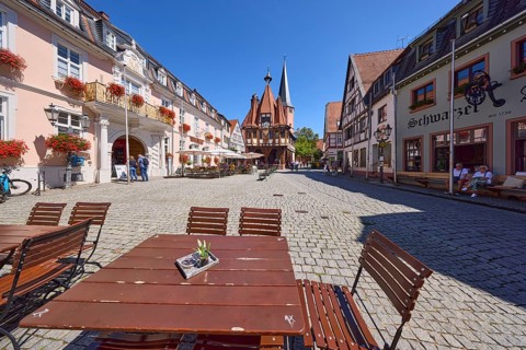 Red tables and chairs of a restaurant and historic town hall on the market square in Michelstadt,