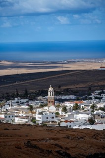 View of town, white houses of Teguise with church tower in dry volcanic landscape, Lanzarote,