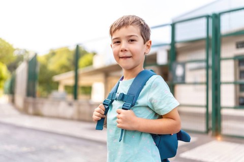 Portrait of a proud boy smiling at camera standing next to school entrance building at first day of