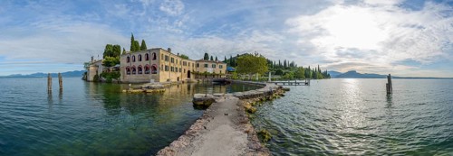 A serene view of a historic lakeside building by a calm lake with a pier extending into the water,