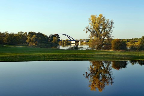 Calm lake with reflections of trees and a bridge behind it under a blue sky, flooded Elbe meadows,