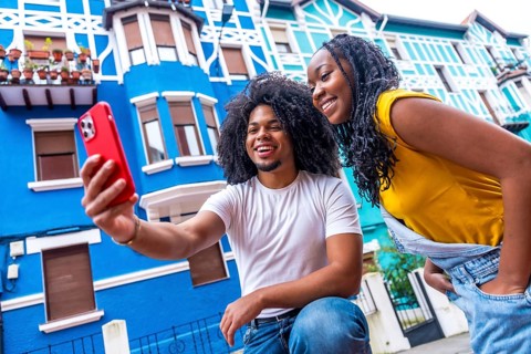 Low angle side view of two young afro friends taking a selfie next to colorful houses