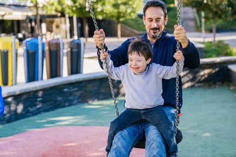 Father and son with Down syndrome, share joyful moments swinging together in a park. Their smiles