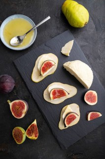 Summer appetizer with pear, cottage cheese, figs and honey on slate board on a black concrete