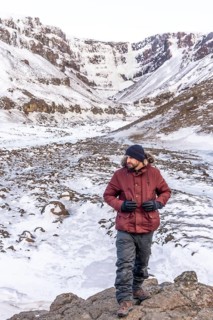 Portrait of a hiker at frozen Hengifoss waterfall in cold Iceland winter, volcanic cliffs