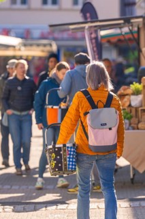 Market visitors in sunny weather, some carrying rucksacks, garden and Keramika Nagold, district of