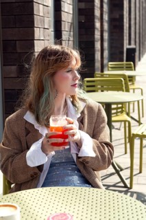 A woman with light hair sips a bright beverage at an outdoor cafe with colorful tables The stylish