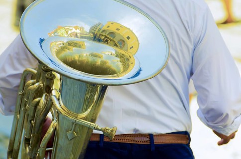 Man Carrying a French Horn Brass with Reflected House Inside His Music Instrument in a Sunny Day in