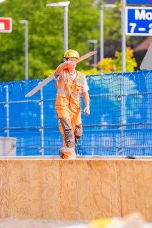 Worker in safety clothing balances a piece of wood on construction site, traffic signs in the