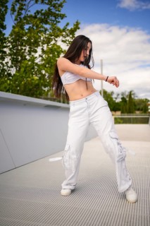 Vertical photo of a cool young caucasian woman in white casual clothes dancing in an urban space