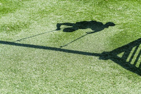 A shadow of a boy swinging joyfully on a playground swing is cast on lush green grass. The sunlit