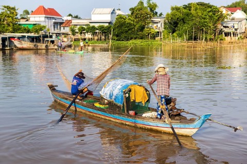A fisherman casts his net from a traditional wooden boat into the Mekong River, Vietnam