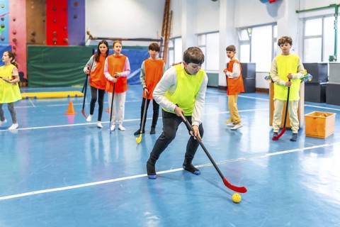 Group of elementary school students learning and playing floor hockey in gym class, promoting