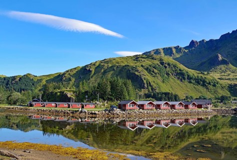 Red wooden cottages reflected in the water, green mountain landscape, Brustranda, Vestvågøy,