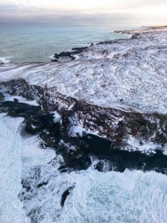 Aerial view of the rugged Icelandic coastline in winter, showcasing the dramatic contrast between