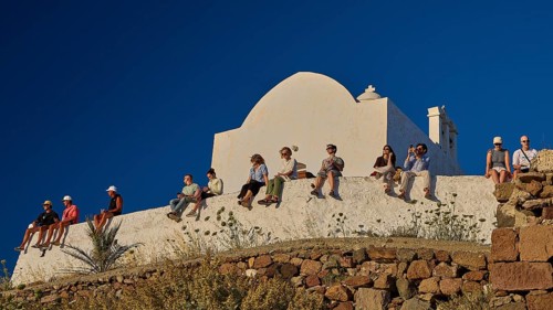 Kastro, Plaka Castle, people sitting on a wall in front of a white church under a clear blue sky,