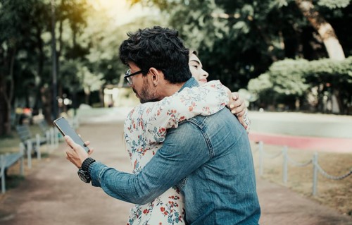Unfaithful man hugging his girlfriend and looking at the cell phone. Concept of unfaithful man