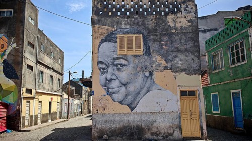 Street with colorful houses and murals, graffiti of a face, mural of 'Cesaria Evora', barefoot