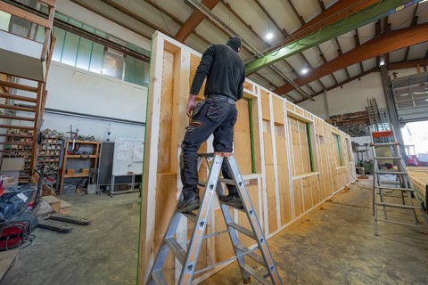 A worker on a ladder in a large workshop works on an interior wall element, façade construction in