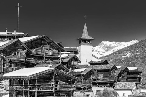 Snow-covered roofs of old farmhouses and barn storage, in the back the large wooden cross and the