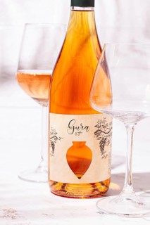 A bottle of rose wine sits on a table next to two empty glasses. The label features a simple design