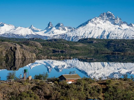The snow-covered Mt. Cerro Castillo is reflected in a lake, small farm by the lake, Patagonia,