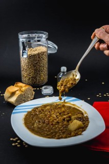 Eating with a spoon inside a plate of Spanish cooked lentils, along with ingredients salt and oil