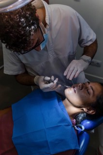 Dentist performing a teeth cleaning on a patient in a clinic setting. The patient is seated in a