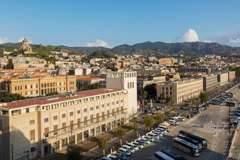High angle view of parking lot with parked sightseeing and tour buses and Messina city skyline,