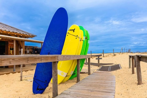 Brightly colored surfboards stand ready for lessons on the sandy beach next to a wooden surf school