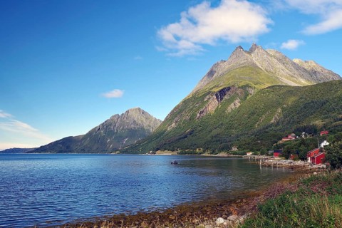 Wooden houses, small fishing boats and steep mountains reflected in the water of a harbour,