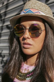 A fashionable young woman poses outdoors, wearing a straw hat, round sunglasses, and a colorful