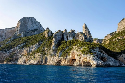 Picturesque rocky coast, cliffs with caves in the morning light, L'Aguglia rock peak, blue sea and