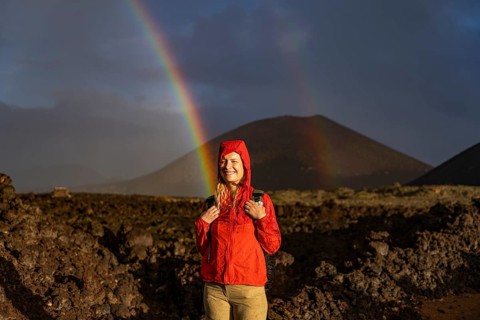 A joyful hiker in a bright red jacket stands in Timanfaya National Park, Lanzarote, with a vivid