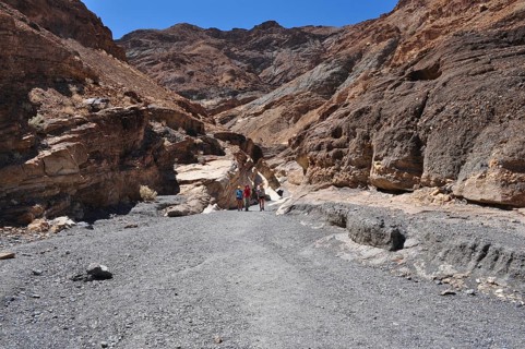 People in a wide rocky gorge under bright blue sky, Death Valley National Park, Mojave Desert,