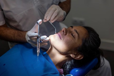 A dentist in gloves performs a teeth cleaning on a patient in a clinic. The dental chair and