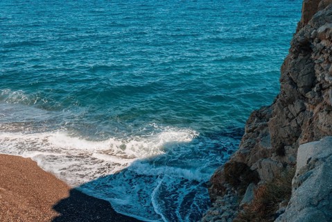 Top view of the black sand, sea, waves and rock at Kamari Beach, Santorini, Turquoise ocean waves