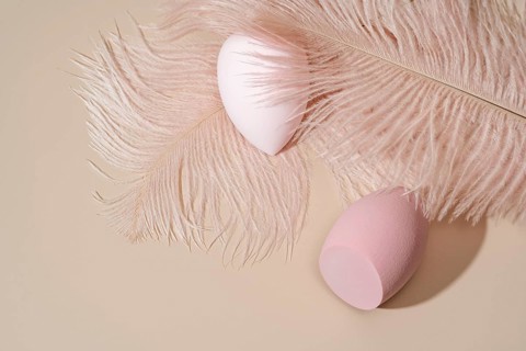 Aesthetic composition featuring two pink cosmetic sponges nestled on a soft beige surface