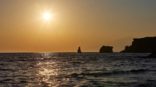 The sun reflects on the calm sea with silhouette-like rocks in the distance, sunset, south of the