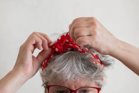 Close up of a senior woman tying a red polka dot scarf as a headband. The scarf adds a retro touch